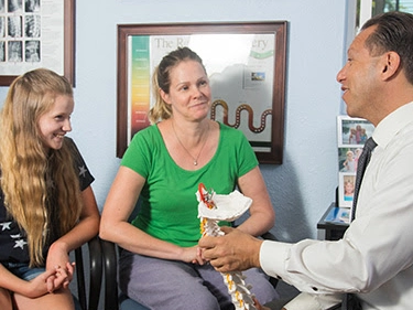Chiropractor showing spine model to family – On Purpose Chiropractic